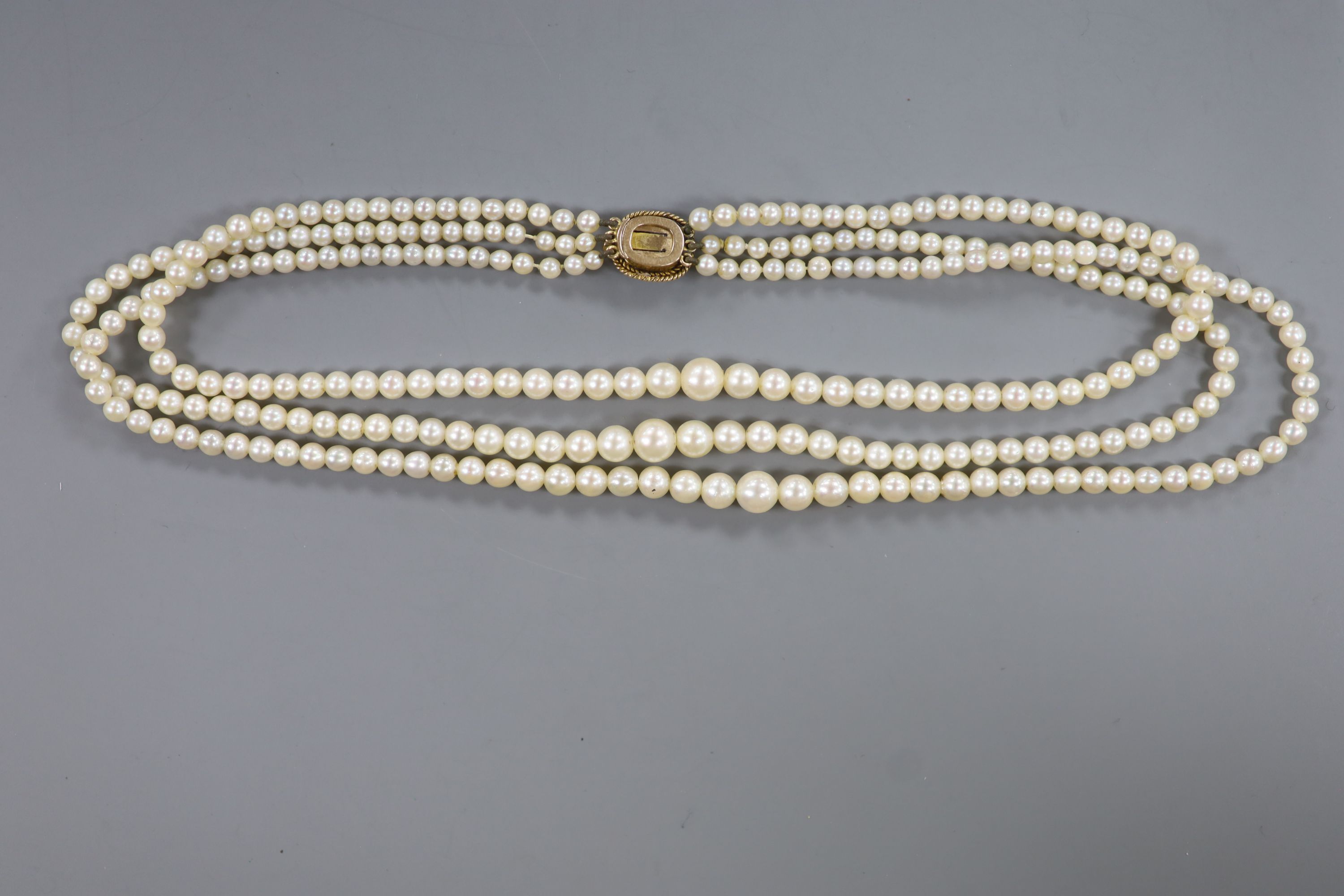 A triple strand graduated cultured pearl choker necklace, with yellow metal and garnet(cracked) set clasp